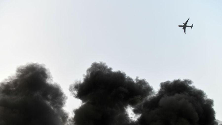 A plane flies above the smoke from a fire inside a warehouse caused by a truck in New Delhi on May 29, 2018. - The fire broke out in a truck which was loaded with plastic material near the rubber godown, no casualties have been reported according to a Fire brigade official. (Photo by CHANDAN KHANNA / AFP)        (Photo credit should read CHANDAN KHANNA/AFP via Getty Images)
