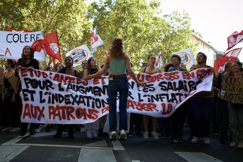 Spanduk bertuliskan 'Mahasiswa dan pekerja untuk menaikkan upah dan untuk mengindeks upah pada inflasi' dibentangkan saat lebih dari 7.000 orang berdemonstrasi di Toulouse selama hari pemogokan nasional, Rabu (19/10/2022).  (Photo by Alain Pitton/NurPhoto via Getty Images)