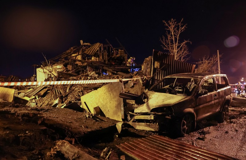 Orang-orang melihat puing-puing pesawat militer Rusia yang jatuh dan menabrak bangunan perumahan di kota Irkutsk, Rusia, Minggu (23/10/2022). Para pejabat mengatakan pesawat itu adalah pesawat tempur Sukhoi Su-30 dalam uji terbang dan menabrak sebuah rumah berlantai dua di kota itu. (REUTERS/Stringer)