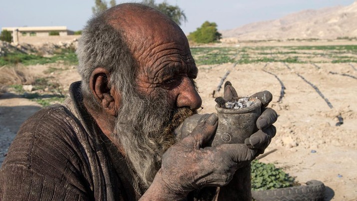 Amou Haji merokok dari pipa saat dia duduk di tanah di pinggiran desa Dezhgah di distrik Dehram di provinsi Fars Iran barat daya, Jumat (28/12/2018). Amou Haji itu dijuluki sebagai 