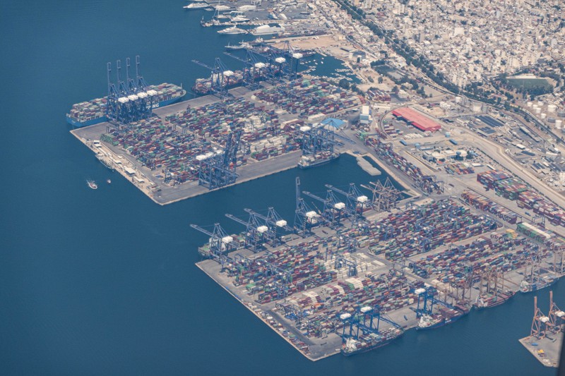 Aerial view from an airplane window of Pireaus port GRPIR. View of large freighter ships, nautical vessels docked while loading - unloading containers and cargo via cranes at the piers of the port at the logistics and container terminal of Perama near the commercial port of Piraeus with thousands of stacked containers. Pireas Port is a logistics hub, the largest Greek port and one of the largest in Europe, serving Athens, Attica and Greece since ancient times. The majority of Port of Piraeus is owned by China COSCO Shipping, the third largest container ship company in the world. As of 2021 the total capacity is at 8,3m TEUs. Piraeus, Greece on August 7, 2022 (Nicolas Economou/NurPhoto via Getty Images) Aerial view from an airplane window of Pireaus port GRPIR. View of large freighter ships, nautical vessels docked while loading - unloading containers and cargo via cranes at the piers of the port at the logistics and container terminal of Perama near the commercial port of Piraeus with thousands of stacked containers. Pireas Port is a logistics hub, the largest Greek port and one of the largest in Europe, serving Athens, Attica and Greece since ancient times. The majority of Port of Piraeus is owned by China COSCO Shipping, the third largest container ship company in the world. As of 2021 the total capacity is at 8,3m TEUs. Piraeus, Greece on August 7, 2022 (Nicolas Economou/NurPhoto via Getty Images)