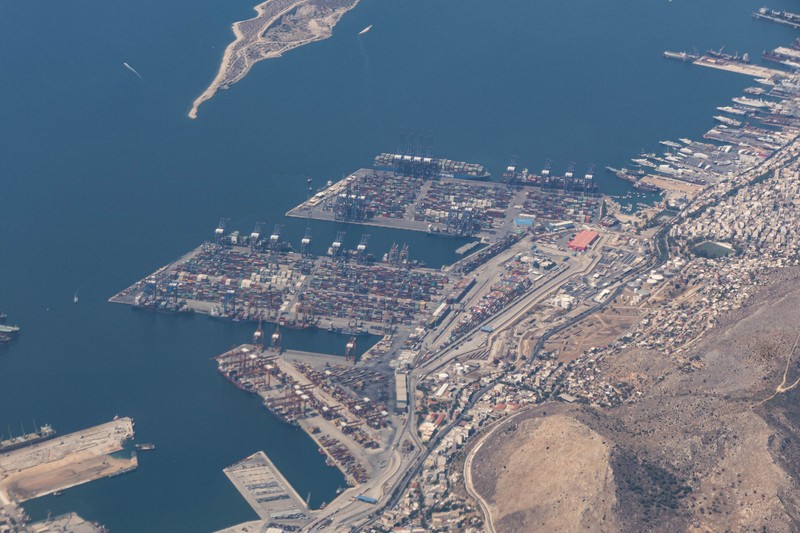 Aerial view from an airplane window of Pireaus port GRPIR. View of large freighter ships, nautical vessels docked while loading - unloading containers and cargo via cranes at the piers of the port at the logistics and container terminal of Perama near the commercial port of Piraeus with thousands of stacked containers. Pireas Port is a logistics hub, the largest Greek port and one of the largest in Europe, serving Athens, Attica and Greece since ancient times. The majority of Port of Piraeus is owned by China COSCO Shipping, the third largest container ship company in the world. As of 2021 the total capacity is at 8,3m TEUs. Piraeus, Greece on August 7, 2022 (Nicolas Economou/NurPhoto via Getty Images)