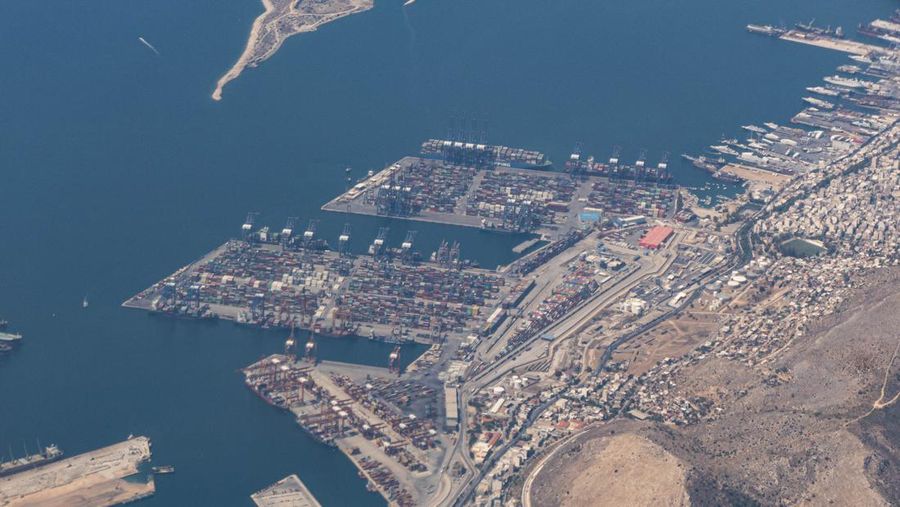 Aerial view from an airplane window of Pireaus port GRPIR. View of large freighter ships, nautical vessels docked while loading - unloading containers and cargo via cranes at the piers of the port at the logistics and container terminal of Perama near the commercial port of Piraeus with thousands of stacked containers. Pireas Port is a logistics hub, the largest Greek port and one of the largest in Europe, serving Athens, Attica and Greece since ancient times. The majority of Port of Piraeus is owned by China COSCO Shipping, the third largest container ship company in the world. As of 2021 the total capacity is at 8,3m TEUs. Piraeus, Greece on August 7, 2022 (Nicolas Economou/NurPhoto via Getty Images)