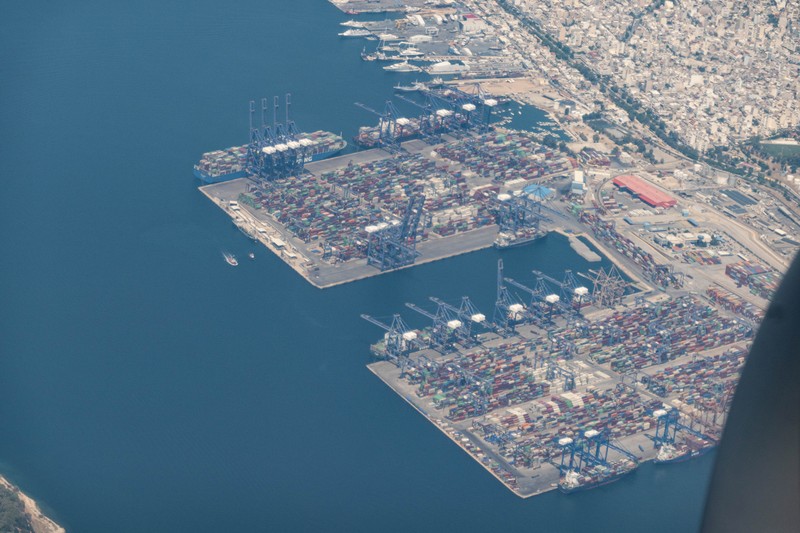 Aerial view from an airplane window of Pireaus port GRPIR. View of large freighter ships, nautical vessels docked while loading - unloading containers and cargo via cranes at the piers of the port at the logistics and container terminal of Perama near the commercial port of Piraeus with thousands of stacked containers. Pireas Port is a logistics hub, the largest Greek port and one of the largest in Europe, serving Athens, Attica and Greece since ancient times. The majority of Port of Piraeus is owned by China COSCO Shipping, the third largest container ship company in the world. As of 2021 the total capacity is at 8,3m TEUs. Piraeus, Greece on August 7, 2022 (Nicolas Economou/NurPhoto via Getty Images)