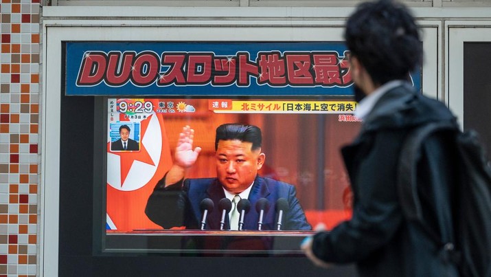 Seorang pria berjalan melewati layar televisi yang menampilkan laporan berita tentang peluncuran rudal terbaru Korea Utara dengan gambar pemimpin Korea Utara, Kim Jong Un, di sepanjang jalan pejalan kaki di Tokyo pada 3 November 2022. (AFP via Getty Images/RICHARD A. BROOKS)