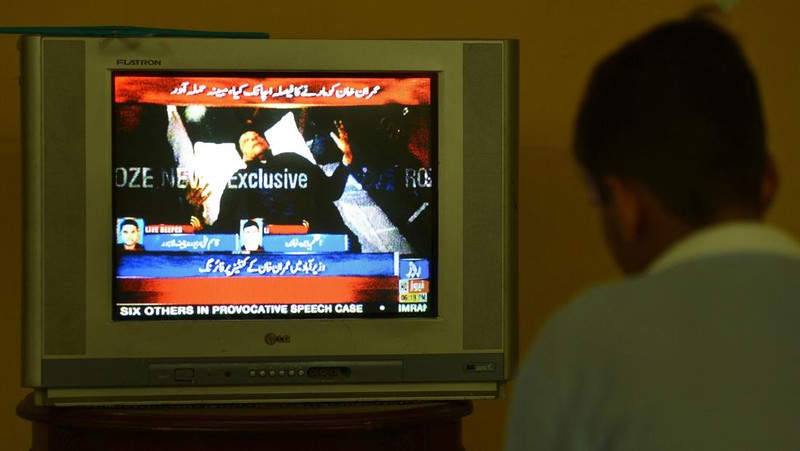 Seorang anak laki-laki menonton saluran televisi yang menayangkan berita tentang mantan perdana menteri Pakistan Imran Khan, di Islamabad pada 3 November 2022. (AFP via Getty Images/FAROOQ NAEEM)