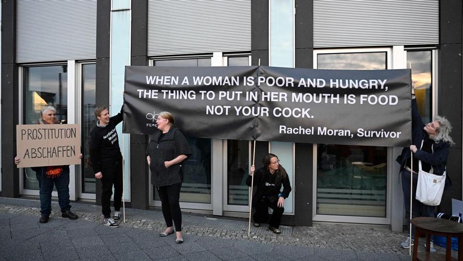 Seorang anggota kelompok aktivis feminis Femen mementaskan pertunjukan di samping seorang demonstran yang memegang poster bertuliskan 'Hapus Prostitusi' di depan gedung BPK (Bundespressekonferenz)  sebelum konferensi pers yang mempresentasikan hasil penelitian tentang prostitusi dan klien mereka di Berlin, Jerman, Selasa (8/11/2022). (Photo by TOBIAS SCHWARZ/AFP via Getty Images)