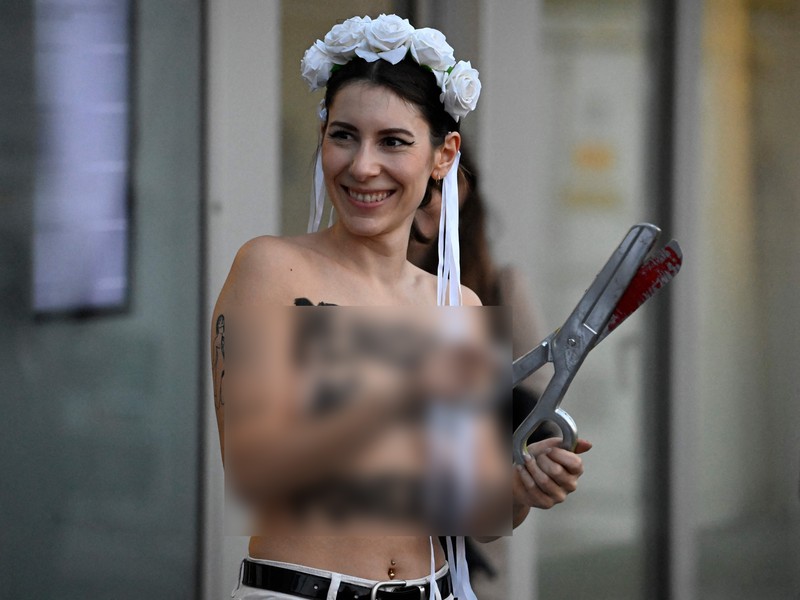 Seorang anggota kelompok aktivis feminis Femen mementaskan pertunjukan di samping seorang demonstran yang memegang poster bertuliskan 'Hapus Prostitusi' di depan gedung BPK (Bundespressekonferenz)  sebelum konferensi pers yang mempresentasikan hasil penelitian tentang prostitusi dan klien mereka di Berlin, Jerman, Selasa (8/11/2022). (Photo by TOBIAS SCHWARZ/AFP via Getty Images)