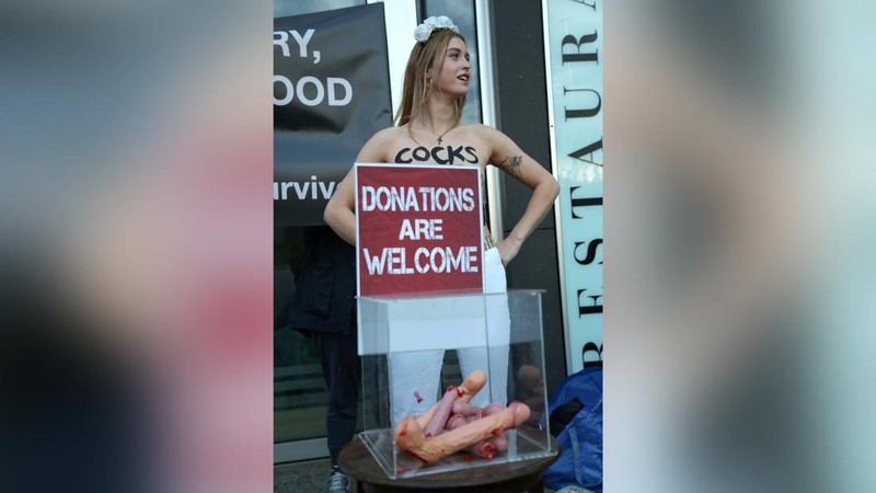 Seorang anggota kelompok aktivis feminis Femen mementaskan pertunjukan di samping seorang demonstran yang memegang poster bertuliskan 'Hapus Prostitusi' di depan gedung BPK (Bundespressekonferenz)  sebelum konferensi pers yang mempresentasikan hasil penelitian tentang prostitusi dan klien mereka di Berlin, Jerman, Selasa (8/11/2022). (Photo by TOBIAS SCHWARZ/AFP via Getty Images)