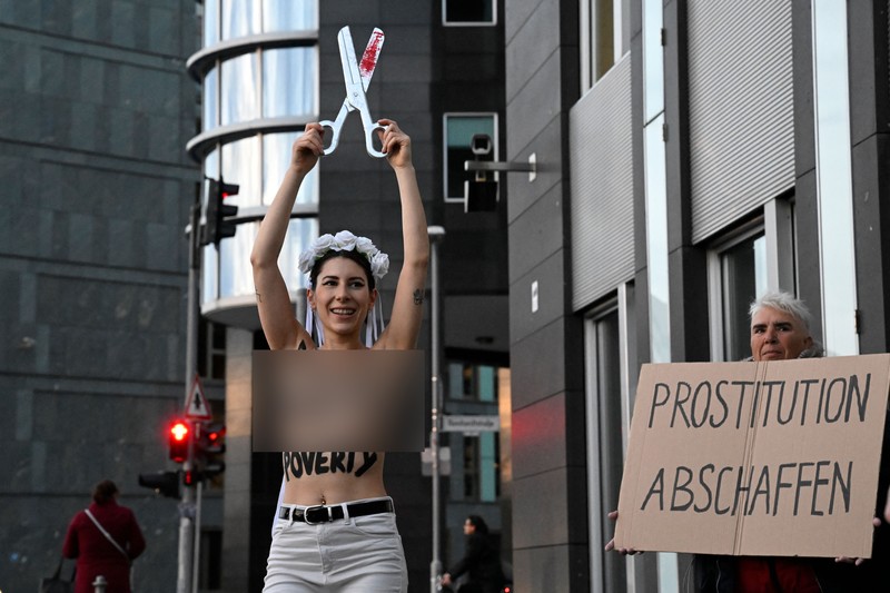 Seorang anggota kelompok aktivis feminis Femen demo Tentang Prostitusi di Jerman Seorang anggota kelompok aktivis feminis Femen mementaskan pertunjukan di samping seorang demonstran yang memegang poster bertuliskan 'Hapus Prostitusi' di depan gedung BPK (Bundespressekonferenz) sebelum konferensi pers yang mempresentasikan hasil penelitian tentang prostitusi dan klien mereka di Berlin, Jerman, Selasa (8/11/2022). (Photo by TOBIAS SCHWARZ/AFP via Getty Images)