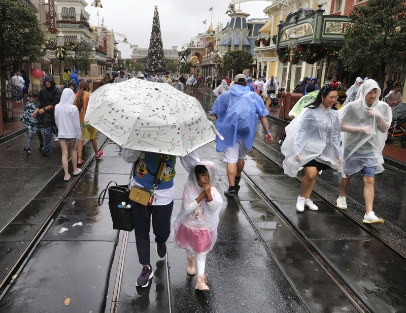 Guests brave the weather in the Magic Kingdom at Walt Disney World in Lake Buena Vista, Fla., Wednesday, Nov. 9, 2022, as conditions deteriorate with the approach of Hurricane Nicole. All 4 Disney parks in Central Florida closed early Wednesday because of the impending storm. (Joe Burbank/Orlando Sentinel via AP)