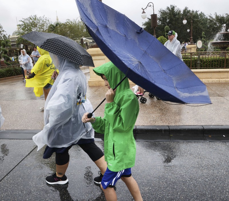 Guests brave the weather in the Magic Kingdom at Walt Disney World in Lake Buena Vista, Fla., Wednesday, Nov. 9, 2022, as conditions deteriorate with the approach of Hurricane Nicole. All 4 Disney parks in Central Florida closed early Wednesday because of the impending storm. (Joe Burbank/Orlando Sentinel via AP)