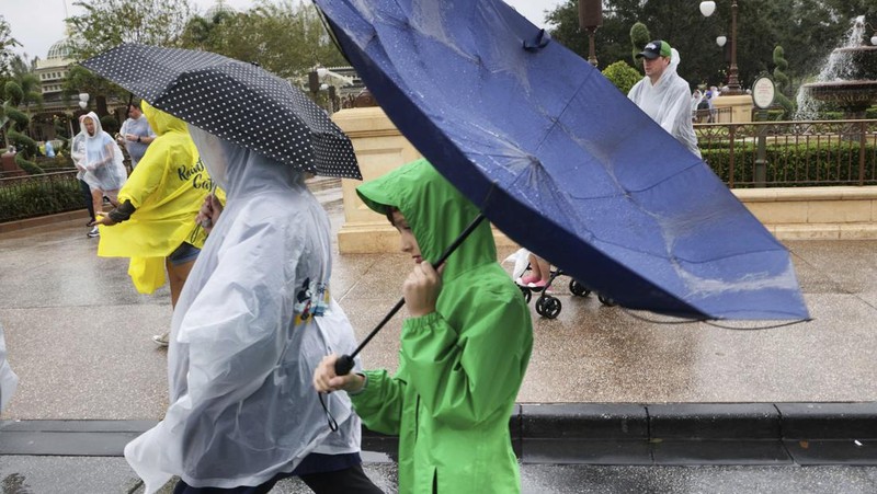 Guests brave the weather in the Magic Kingdom at Walt Disney World in Lake Buena Vista, Fla., Wednesday, Nov. 9, 2022, as conditions deteriorate with the approach of Hurricane Nicole. All 4 Disney parks in Central Florida closed early Wednesday because of the impending storm. (Joe Burbank/Orlando Sentinel via AP)