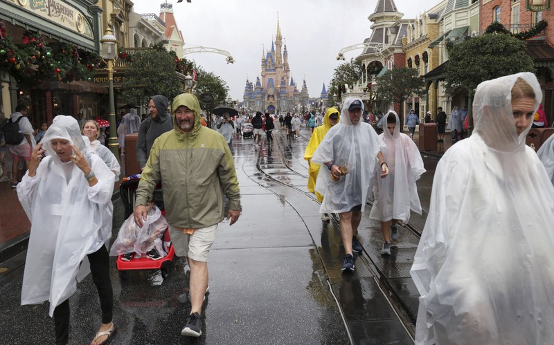 Guests brave the weather in the Magic Kingdom at Walt Disney World in Lake Buena Vista, Fla., Wednesday, Nov. 9, 2022, as conditions deteriorate with the approach of Hurricane Nicole. All 4 Disney parks in Central Florida closed early Wednesday because of the impending storm. (Joe Burbank/Orlando Sentinel via AP)