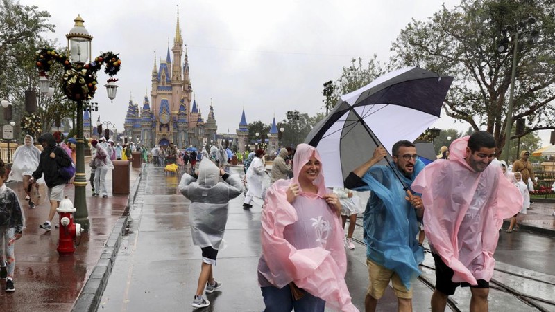 Guests brave the weather in the Magic Kingdom at Walt Disney World in Lake Buena Vista, Fla., Wednesday, Nov. 9, 2022, as conditions deteriorate with the approach of Hurricane Nicole. All 4 Disney parks in Central Florida closed early Wednesday because of the impending storm. (Joe Burbank/Orlando Sentinel via AP)