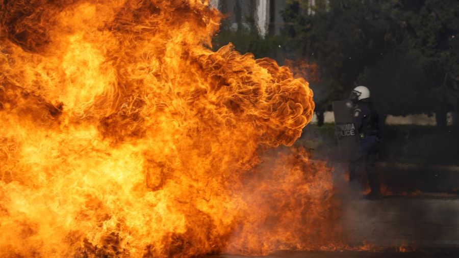 Sebuah bom molotov meledak di dekat polisi anti huru hara di luar Parlemen Yunani selama bentrokan di Athena, Yunani, Rabu, 9 November 2022. Ribuan pengunjuk rasa berbaris melalui jalan-jalan Athena dan kota Thessaloniki di Yunani utara sebagai pekerja publik dan beberapa sektor swasta meninggalkan pekerjaan untuk pemogokan umum 24 jam terhadap kenaikan harga. (Foto AP/Petros Giannakouris)