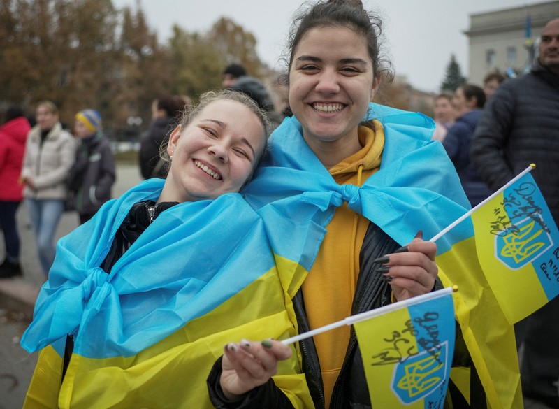 1244739977 People hold Ukrainian flags as they gather to celebrate the liberation of their town in Kherson, on November 12, 2022, amid Russia's invasion of Ukraine. - On November 11, 2022, Russia said it had pulled back more than 30,000 troops in the southern region, with Ukrainian President Volodymyr Zelensky declaring Kherson