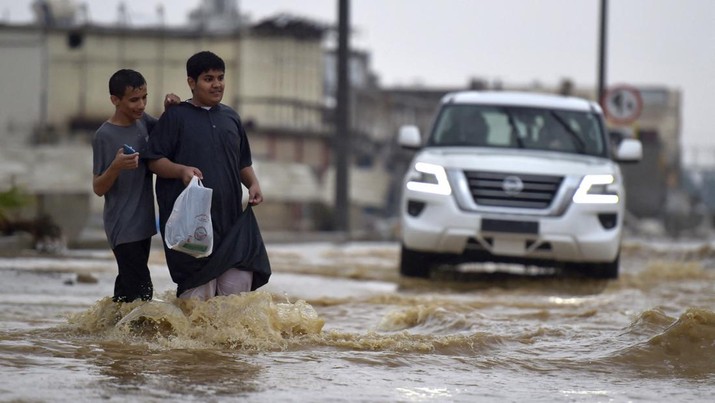 Pemuda berjalan di jalan yang banjir setelah hujan lebat di kota pesisir Saudi Jeddah pada 24 November 2022 yang menunda penerbangan, memaksa penangguhan sekolah dan menutup jalan ke Mekah, kota paling suci Islam. - Jeddah, kota berpenduduk sekitar empat juta orang yang terletak di Laut Merah, sering disebut sebagai 