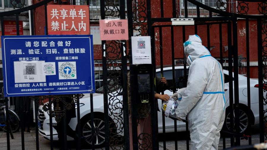 A worker in a protective suit passes a delivery good to a resident through a gate of a residential compound that is still under lockdown, following a coronavirus disease (COVID-19) outbreak, in Chaoyang District of Beijing, China November 26, 2022. REUTERS/Tingshu Wang