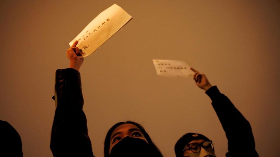 Orang-orang melakukan aksi dengan memegang kertas putih untuk memprotes pembatasan penyakit coronavirus (COVID-19), saat mereka memperingati para korban kebakaran di Urumqi, ketika wabah penyakit virus corona meningkat di Beijing, China, Minggu (27/11/2022). Warga melakukan aksi protes terhadap pelebaran aturan lockdown akibat kasus COVID-19 telah mencapai rekor tertinggi selama berhari-hari.  (REUTERS/Thomas Peter)