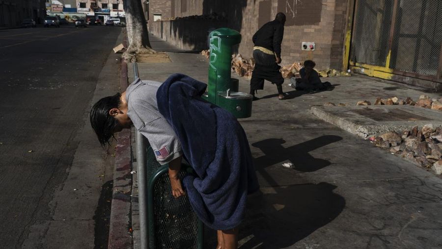 Seorang wanita tunawisma yang sakit jiwa bersandar di pagar setelah membasahi rambutnya di air mancur minum di daerah Skid Row Los Angeles, Senin (23/5/2022) RUU kontroversial yang ditandatangani oleh Gubernur Gavin Newsom dapat memperbaikinya dengan memaksa orang yang menderita gangguan jiwa berat ke dalam pengobatan. Tetapi mereka perlu didiagnosis dengan kelainan tertentu seperti skizofrenia dan kecanduan saja tidak memenuhi syarat. (AP Photo/Jae C. Hong)