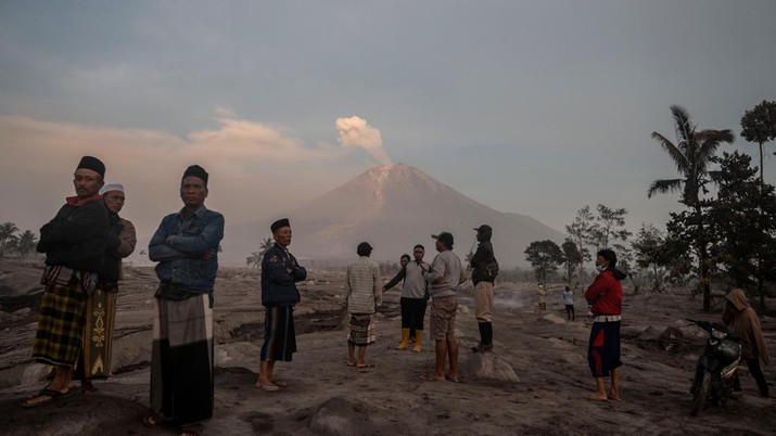 1245371478 People stand before Mount Semeru following a volcanic eruption at Kajar Kuning village in Lumajang on December 5, 2022. - Indonesia's Mount Semeru erupted on December 4 spewing hot ash clouds a mile high and rivers of lava down its side while sparking the evacuation of nearly 2,000 people exactly one year after its last major eruption killed dozens. (Photo by JUNI KRISWANTO / AFP) (Photo by JUNI KRISWANTO/AFP via Getty Images)