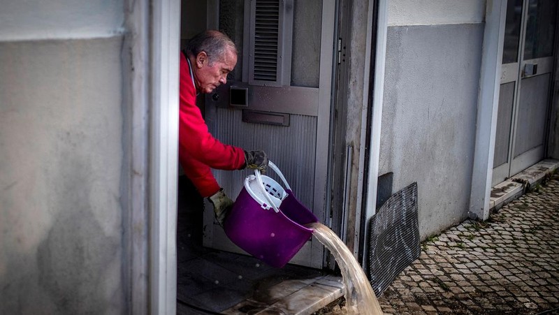 Seorang pria mencoba membuang air berlumpur setelah banjir di Lisbon pada 8 Desember 2022. - Satu orang meninggal tadi malam akibat banjir di wilayah Lisbon, dilanda hujan lebat, kata dinas pertahanan sipil. (CARLOS COSTA/AFP via Getty Images)