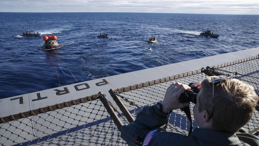 Kapsul Orion NASA berjalan menuju USS Portland (LPD 27) setelah berhasil diamankan oleh tim NASA dan Angkatan Laut AS di lepas pantai Baja California, Meksiko, pada 11 Desember 2022. - Orion diluncurkan 16 November dengan roket Artemis untuk misi 25 hari ke Bulan. Tujuan utama dari misi ini adalah untuk menguji pelindung panas Orion apa cocok untuk manusia berada di dalamnya. (CAROLINE BREHMAN/POOL/AFP via Getty Images)