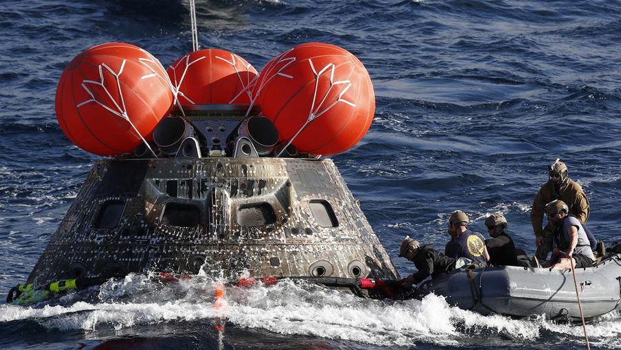 Kapsul Orion NASA berjalan menuju USS Portland (LPD 27) setelah berhasil diamankan oleh tim NASA dan Angkatan Laut AS di lepas pantai Baja California, Meksiko, pada 11 Desember 2022. - Orion diluncurkan 16 November dengan roket Artemis untuk misi 25 hari ke Bulan. Tujuan utama dari misi ini adalah untuk menguji pelindung panas Orion apa cocok untuk manusia berada di dalamnya. (CAROLINE BREHMAN/POOL/AFP via Getty Images)