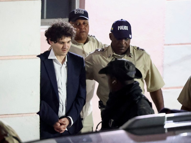 Sam Bankman-Fried, yang mendirikan dan memimpin FTX sampai krisis likuiditas memaksa pertukaran cryptocurrency untuk menyatakan kebangkrutan, dikawal keluar dari gedung Pengadilan Magistrate setelah penangkapannya, di Nassau, Bahamas 13 Desember 2022. (REUTERS/DANTE CARRER)