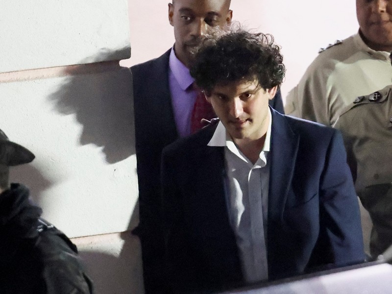 Sam Bankman-Fried, yang mendirikan dan memimpin FTX sampai krisis likuiditas memaksa pertukaran cryptocurrency untuk menyatakan kebangkrutan, dikawal keluar dari gedung Pengadilan Magistrate setelah penangkapannya, di Nassau, Bahamas 13 Desember 2022. (REUTERS/DANTE CARRER)