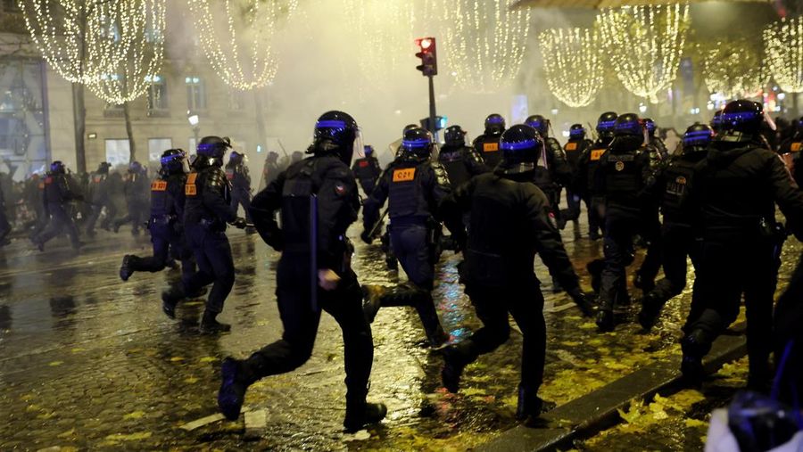 Seorang petugas polisi menendang seseorang setelah pertandingan final sepak bola Piala Dunia antara Argentina dan Prancis di jalan Champs-Elysees, Paris, Minggu (18/12/2022). Argentina telah memenangkan Piala Dunia dengan mengalahkan Prancis 4-2 dalam adu penalti di final. (AP Photo/Thibault Camus)
