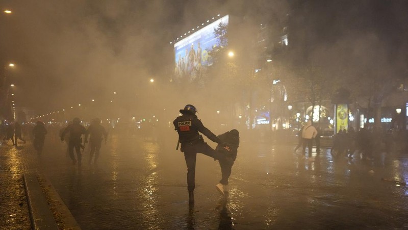 Seorang petugas polisi menendang seseorang setelah pertandingan final sepak bola Piala Dunia antara Argentina dan Prancis di jalan Champs-Elysees, Paris, Minggu (18/12/2022). Argentina telah memenangkan Piala Dunia dengan mengalahkan Prancis 4-2 dalam adu penalti di final. (AP Photo/Thibault Camus)
