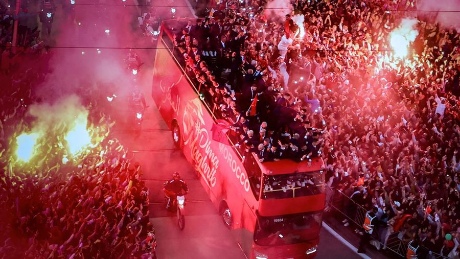 Pendukung bersorak dan menyalakan suar saat tim sepak bola nasional Maroko tiba di pusat ibu kota Rabat, pada 20 Desember 2022, setelah Piala Dunia Qatar 2022. (FADEL SENNA/AFP via Getty Images)