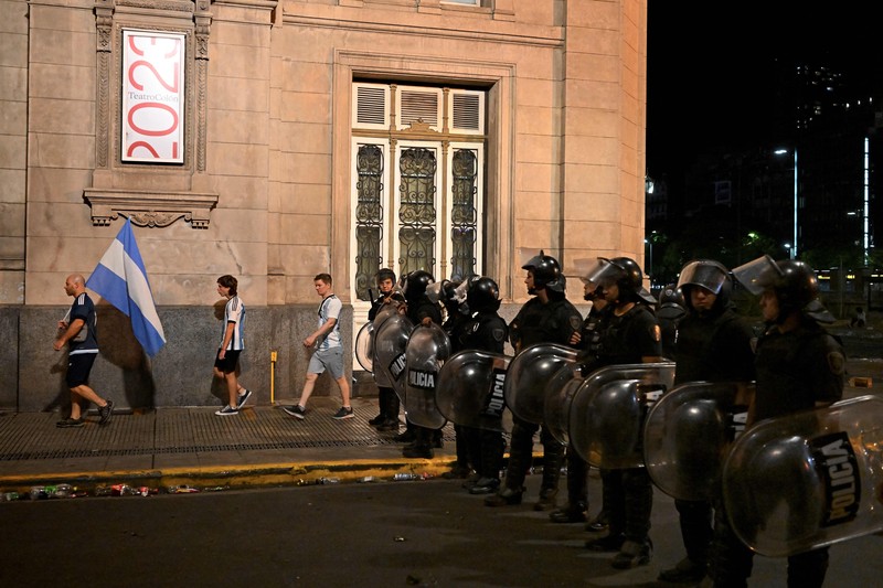 Seorang polisi anti huru hara menghadapi seorang penggemar Argentina selama bentrokan setelah perayaan kedatangan tim dari turnamen Piala Dunia Qatar 2022, yang membuat jutaan orang kecewa ketika parade bus beratap terbuka harus ditinggalkan karena kerumunan besar, pada 20 Desember, 2022, di sekitar Obelisk di Buenos Aires.  (LUIS ROBAYO/AFP via Getty Images)