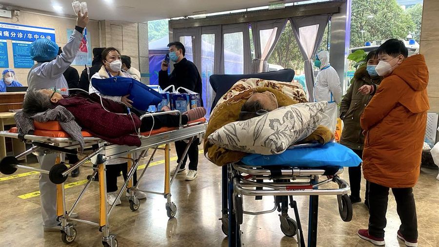 Pengemudi ambulans menurunkan pasien di luar klinik demam yang merawat pasien COVID-19 di Beijing, China, Rabu (21/12/2022). Kondisi pandemi Covid-19 di China terus memburuk seiring dengan berakhirnya kebijakan penguncian ketat di seluruh negeri. (Photo by Kevin Frayer/Getty Images)