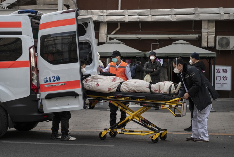 Pengemudi ambulans menurunkan pasien di luar klinik demam yang merawat pasien COVID-19 di Beijing, China, Rabu (21/12/2022). Kondisi pandemi Covid-19 di China terus memburuk seiring dengan berakhirnya kebijakan penguncian ketat di seluruh negeri. (Photo by Kevin Frayer/Getty Images)