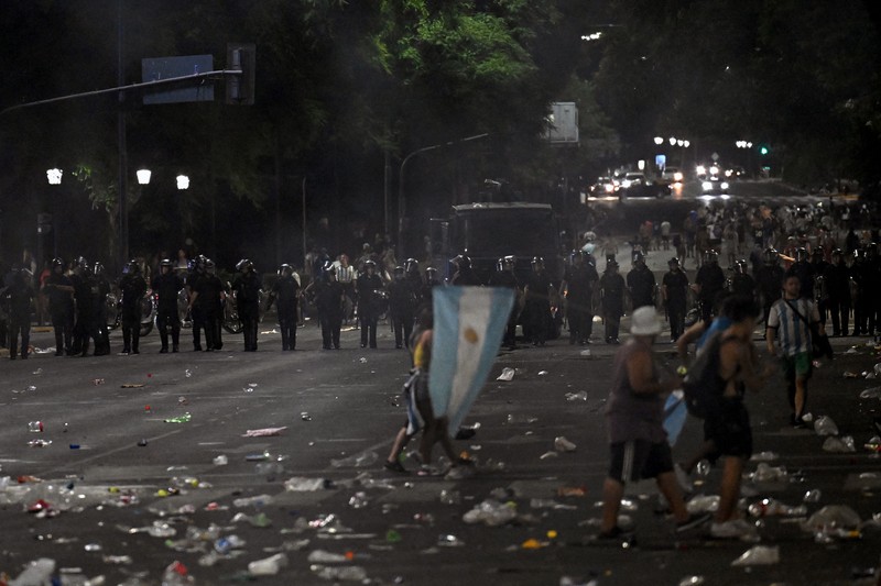 Seorang polisi anti huru hara menghadapi seorang penggemar Argentina selama bentrokan setelah perayaan kedatangan tim dari turnamen Piala Dunia Qatar 2022, yang membuat jutaan orang kecewa ketika parade bus beratap terbuka harus ditinggalkan karena kerumunan besar, pada 20 Desember, 2022, di sekitar Obelisk di Buenos Aires.  (LUIS ROBAYO/AFP via Getty Images)