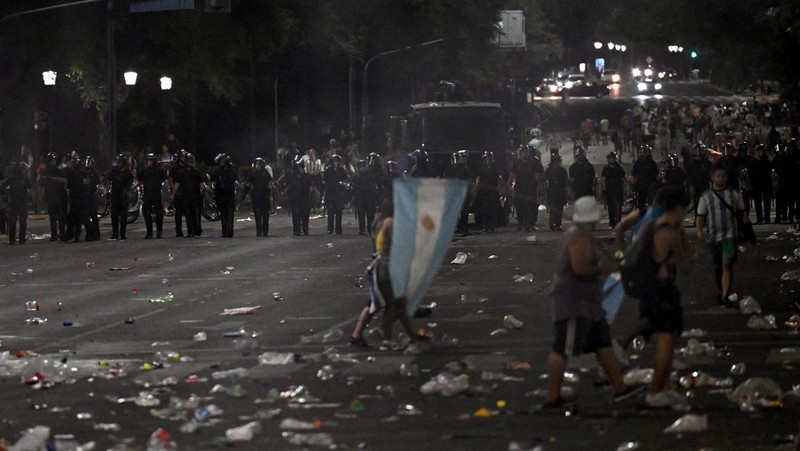 Seorang polisi anti huru hara menghadapi seorang penggemar Argentina selama bentrokan setelah perayaan kedatangan tim dari turnamen Piala Dunia Qatar 2022, yang membuat jutaan orang kecewa ketika parade bus beratap terbuka harus ditinggalkan karena kerumunan besar, pada 20 Desember, 2022, di sekitar Obelisk di Buenos Aires.  (LUIS ROBAYO/AFP via Getty Images)