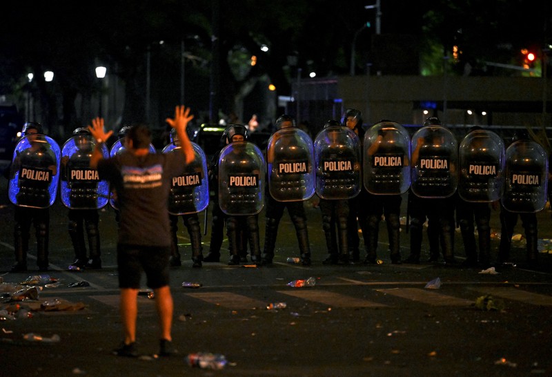 Seorang polisi anti huru hara menghadapi seorang penggemar Argentina selama bentrokan setelah perayaan kedatangan tim dari turnamen Piala Dunia Qatar 2022, yang membuat jutaan orang kecewa ketika parade bus beratap terbuka harus ditinggalkan karena kerumunan besar, pada 20 Desember, 2022, di sekitar Obelisk di Buenos Aires. Seorang polisi anti huru hara menghadapi seorang penggemar Argentina selama bentrokan setelah perayaan kedatangan tim dari turnamen Piala Dunia Qatar 2022, yang membuat jutaan orang kecewa ketika parade bus beratap terbuka harus ditinggalkan karena kerumunan besar, pada 20 Desember, 2022, di sekitar Obelisk di Buenos Aires. (LUIS ROBAYO/AFP via Getty Images)