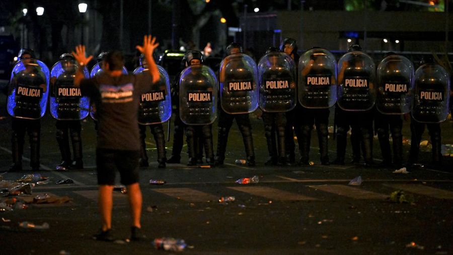 Seorang polisi anti huru hara menghadapi seorang penggemar Argentina selama bentrokan setelah perayaan kedatangan tim dari turnamen Piala Dunia Qatar 2022, yang membuat jutaan orang kecewa ketika parade bus beratap terbuka harus ditinggalkan karena kerumunan besar, pada 20 Desember, 2022, di sekitar Obelisk di Buenos Aires.  (LUIS ROBAYO/AFP via Getty Images)