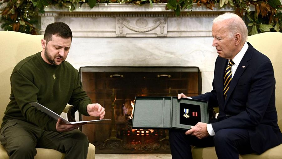 Presiden Ukraina Volodymyr Zelensky mempersembahkan medali militer Ukraina (The Cross for Military Merit) kepada Presiden AS Joe Biden di Oval Office Gedung Putih, di Washington, DC pada 21 Desember 2022. Zelenskyy menyebutkan medali khusus ini diberikan lebih awal dari ini. tahun kepada seorang perwira Ukraina untuk prestasi luar biasa di medan perang. Petugas itu bertemu awal pekan ini dengan Presiden Zelenskyy di Bakhmut dan memintanya untuk memberikan medalinya kepada Presiden Biden sebagai tanda terima kasihnya yang mendalam. Petugas itu juga menulis surat kepada Presiden Biden yang menyatakan penghargaan Ukraina atas bantuan Amerika yang membantu banyak orang di Ukraina tetap hidup. Zelensky berada di Washington untuk bertemu dengan Presiden AS Joe Biden dan berpidato di Kongres -- perjalanan pertamanya ke luar negeri sejak Rusia menginvasi pada Februari. (BRENDAN SMIALOWSKI/AFP via Getty Images)