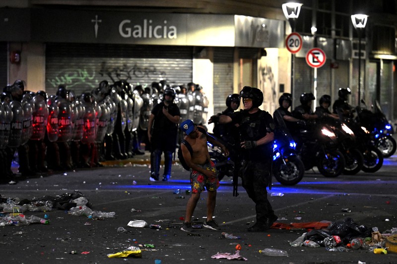 Seorang polisi anti huru hara menghadapi seorang penggemar Argentina selama bentrokan setelah perayaan kedatangan tim dari turnamen Piala Dunia Qatar 2022, yang membuat jutaan orang kecewa ketika parade bus beratap terbuka harus ditinggalkan karena kerumunan besar, pada 20 Desember, 2022, di sekitar Obelisk di Buenos Aires.  (LUIS ROBAYO/AFP via Getty Images)