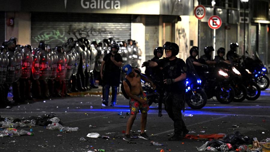 Seorang polisi anti huru hara menghadapi seorang penggemar Argentina selama bentrokan setelah perayaan kedatangan tim dari turnamen Piala Dunia Qatar 2022, yang membuat jutaan orang kecewa ketika parade bus beratap terbuka harus ditinggalkan karena kerumunan besar, pada 20 Desember, 2022, di sekitar Obelisk di Buenos Aires.  (LUIS ROBAYO/AFP via Getty Images)