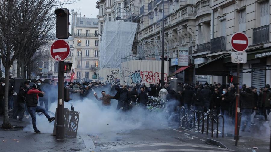 Police officers stand in a cloud of teargas as they clashes with members of Kurdish community near the crime scene where a shooting took place in Paris, Friday, Dec. 23, 2022. Skirmishes erupted in the neighbourhood a few hours after the shooting, as members of the Kurdish community shouted slogans against the Turkish government, and police fired tear gas to disperse an increasingly agitated crowd. A shooting targeting a Kurdish cultural center in Paris Friday left three people dead and three others wounded. (AP Photo/Lewis Joly)