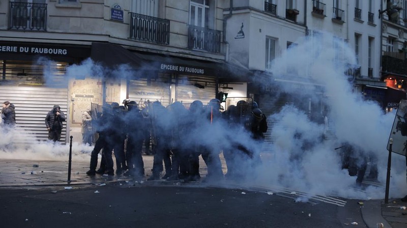 Police officers stand in a cloud of teargas as they clashes with members of Kurdish community near the crime scene where a shooting took place in Paris, Friday, Dec. 23, 2022. Skirmishes erupted in the neighbourhood a few hours after the shooting, as members of the Kurdish community shouted slogans against the Turkish government, and police fired tear gas to disperse an increasingly agitated crowd. A shooting targeting a Kurdish cultural center in Paris Friday left three people dead and three others wounded. (AP Photo/Lewis Joly)