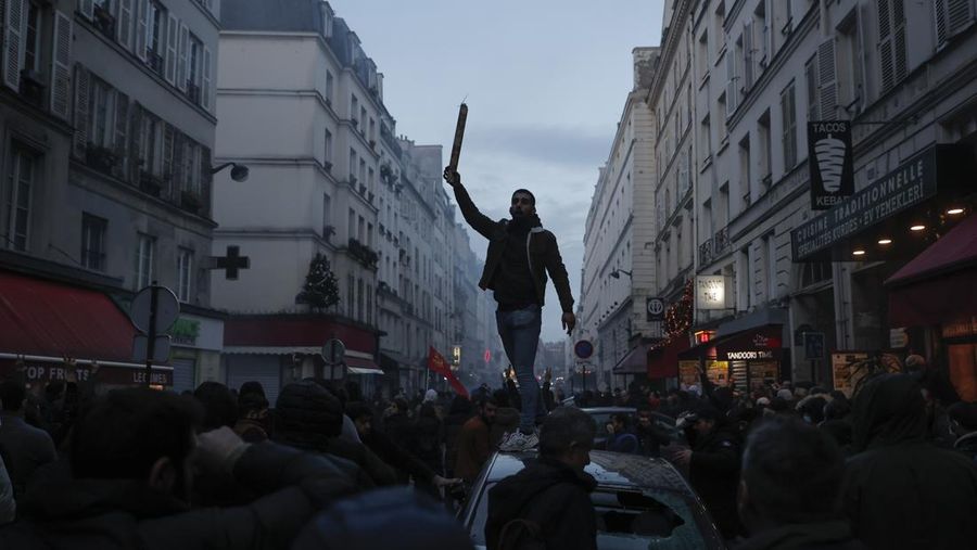 A members of Kurdish community stands on the top of a car during clashes with police officers near the crime scene where a shooting took place in Paris, Friday, Dec. 23, 2022. Skirmishes erupted in the neighbourhood a few hours after the shooting, as members of the Kurdish community shouted slogans against the Turkish government, and police fired tear gas to disperse an increasingly agitated crowd. A shooting targeting a Kurdish cultural center in Paris Friday left three people dead and three others wounded. (AP Photo/Lewis Joly)