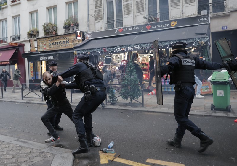 Police officers stand in a cloud of teargas as they clashes with members of Kurdish community near the crime scene where a shooting took place in Paris, Friday, Dec. 23, 2022. Skirmishes erupted in the neighbourhood a few hours after the shooting, as members of the Kurdish community shouted slogans against the Turkish government, and police fired tear gas to disperse an increasingly agitated crowd. A shooting targeting a Kurdish cultural center in Paris Friday left three people dead and three others wounded. (AP Photo/Lewis Joly)