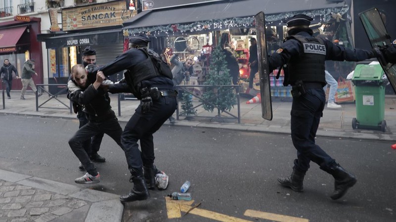 Police officers stand in a cloud of teargas as they clashes with members of Kurdish community near the crime scene where a shooting took place in Paris, Friday, Dec. 23, 2022. Skirmishes erupted in the neighbourhood a few hours after the shooting, as members of the Kurdish community shouted slogans against the Turkish government, and police fired tear gas to disperse an increasingly agitated crowd. A shooting targeting a Kurdish cultural center in Paris Friday left three people dead and three others wounded. (AP Photo/Lewis Joly)