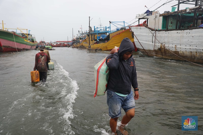 Banjir Rob di Pelabuhan Muara Baru, Anak Buah Kapal (ABK) melintasi banjir rob saat cuaca buruk di Pelabuhan Muara Baru, Penjaringan, Jakarta Utara, Rabu (28/12/2022). Badan Meteorologi Klimatologi dan Geofisika (BMKG) menyampaikan ada potensi cuaca ekstrem terjadi di sejumlah wilayah di Indonesia. (CNBC Indonesia/ Muhammad Sabki)